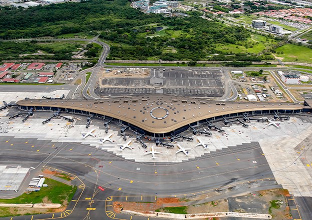 Image shows an airport terminal that is shaped like an aircraft ring. There are many planes parked around the terminal. 